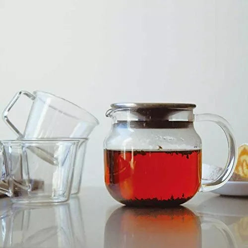 Comandante coffee grinder next to a clear Kinto One Touch Teapot 460ml, showcasing the grinder's handle and the teapot's glass body.