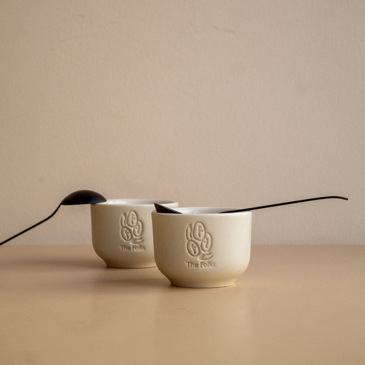 Ceramic mug featuring The Folks logo next to a Comandante coffee grinder on a wooden surface.