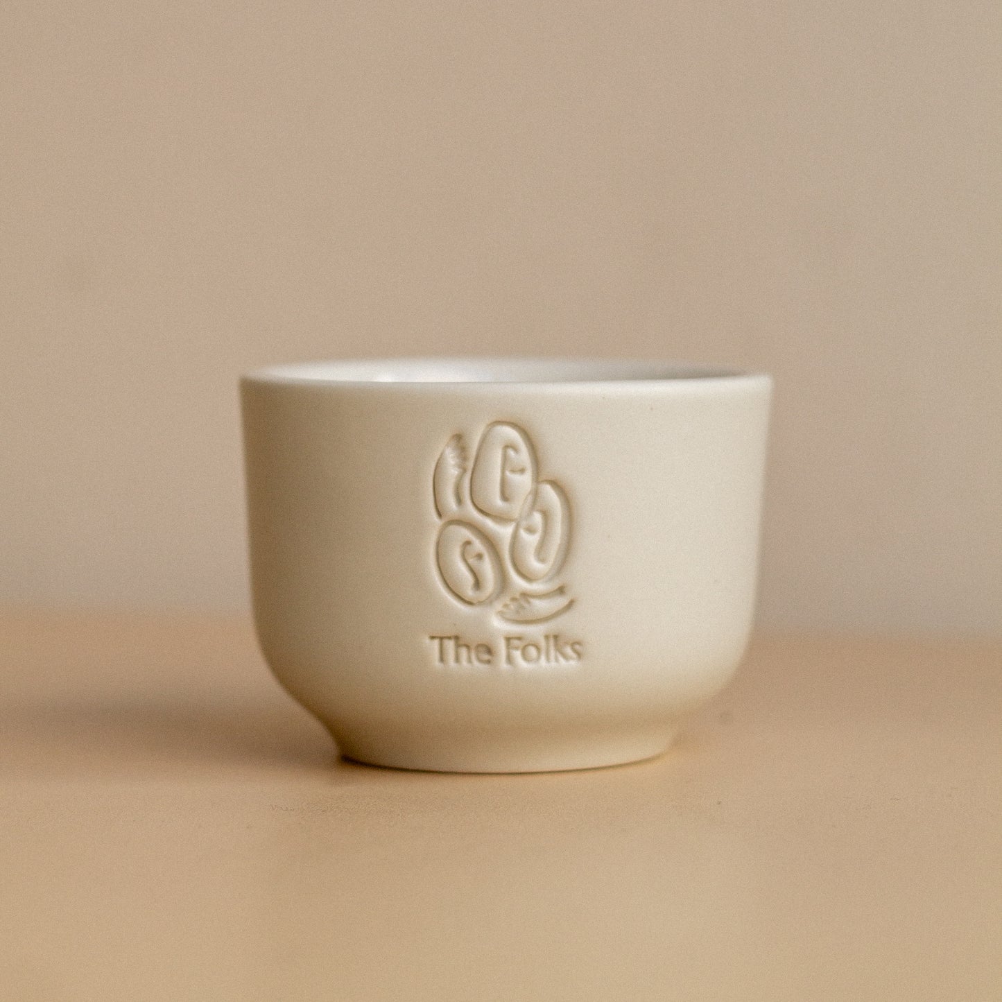 Ceramic mug from The Folks next to a Comandante coffee grinder on a wooden surface.