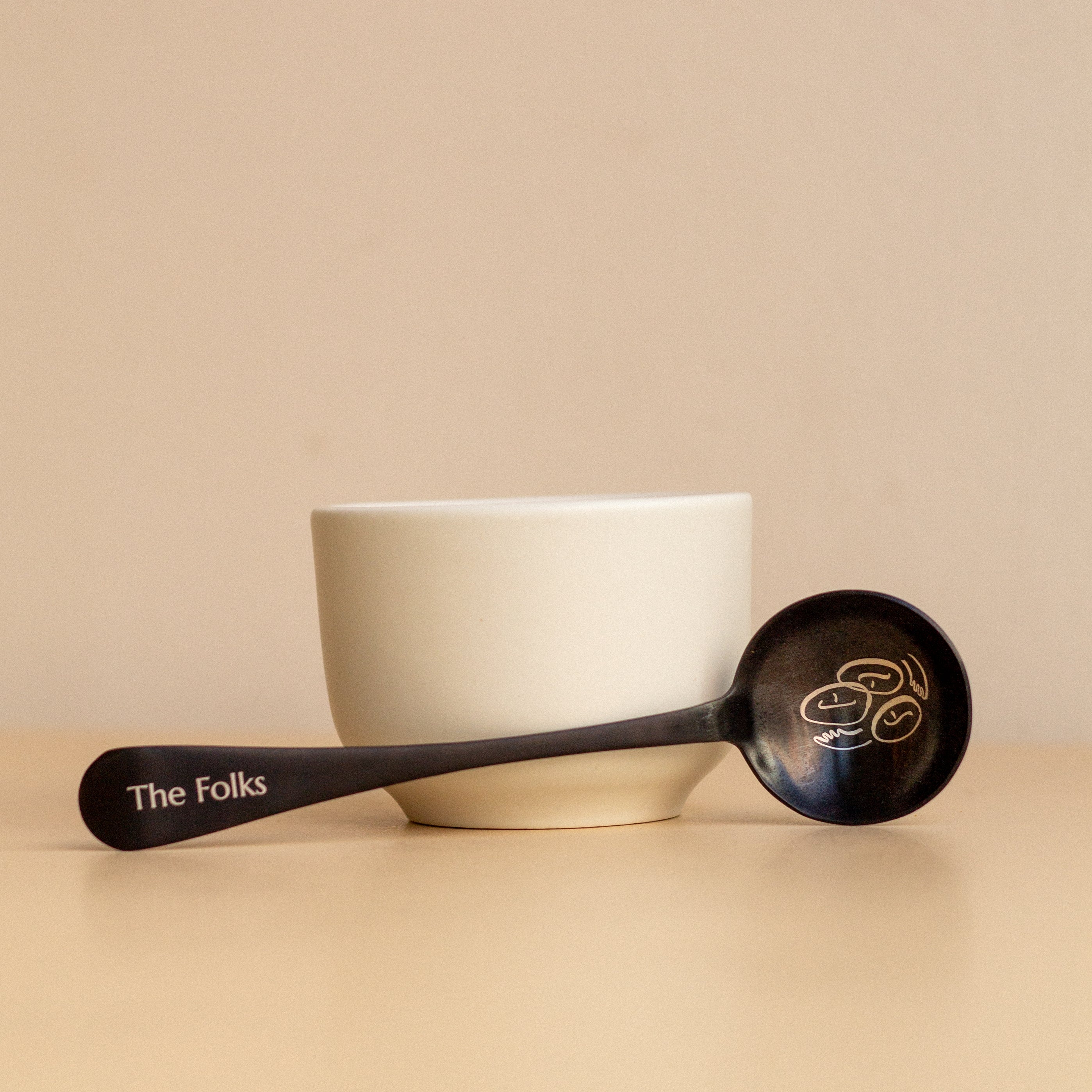 Comandante coffee grinder with a The Folks cupping spoon, featuring a sleek design and durable build for precise coffee brewing.
