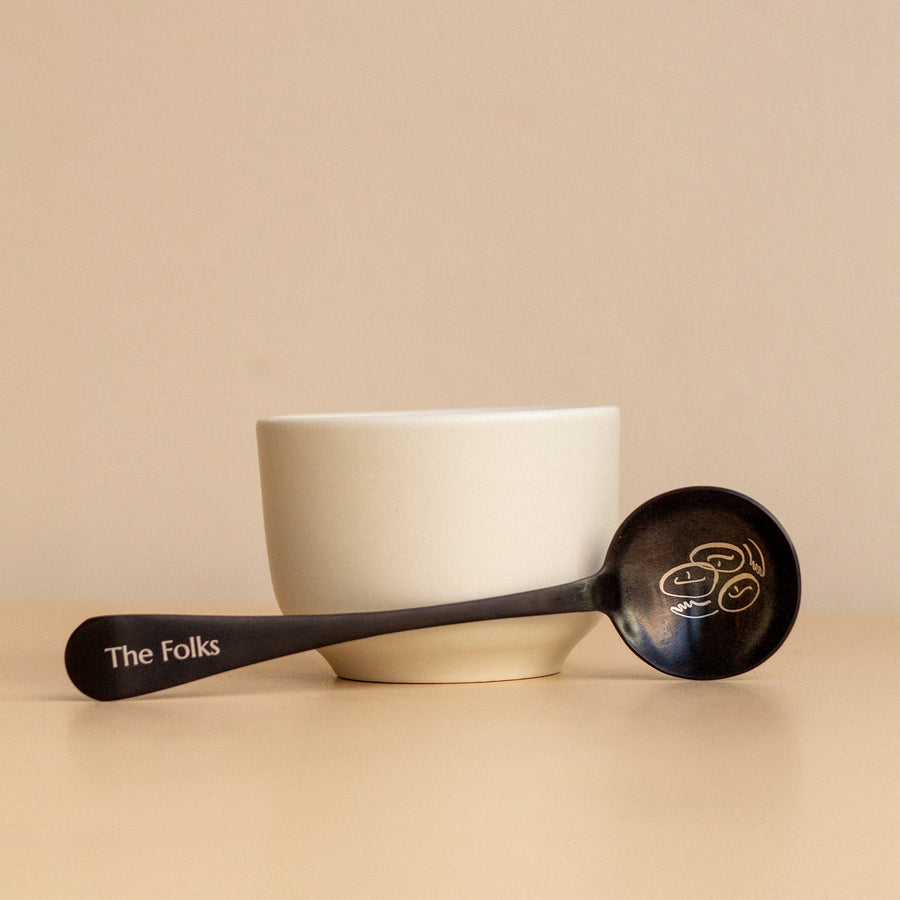 Comandante coffee grinder with a The Folks cupping spoon, featuring a sleek design and durable build for precise coffee brewing.