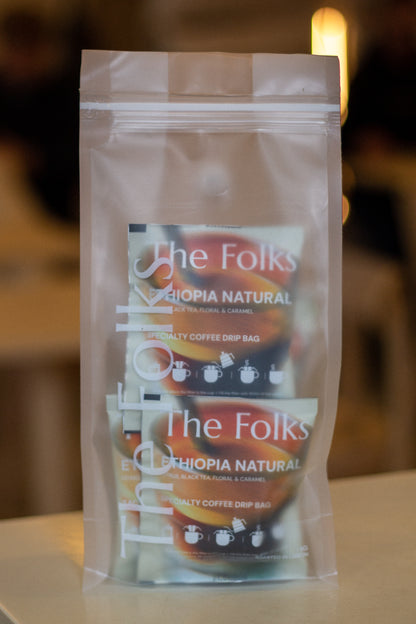Bag of The Folks Colombia drip coffee beans with Flor de Azafrán label, showcasing fresh coffee beans in a natural setting.